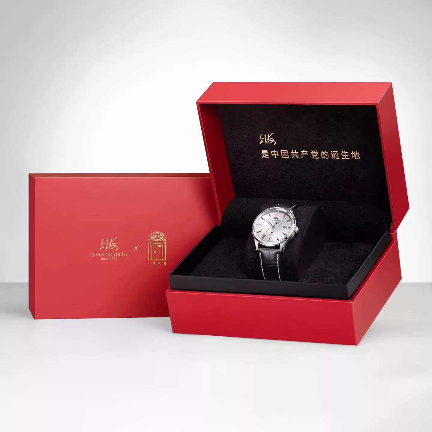 A red watch presentation box shown open with a wristwatch inside, alongside a closed matching red box. The watch has a silver-toned case and a dark strap.